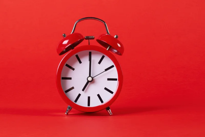 Red classic alarm clock with white face and black hands on red background