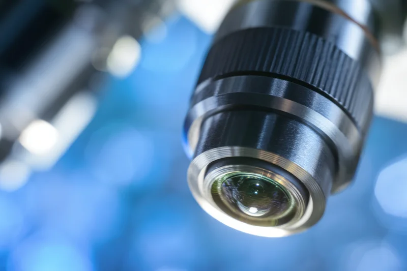 Close-up of a microscope objective lens with a blurred blue background