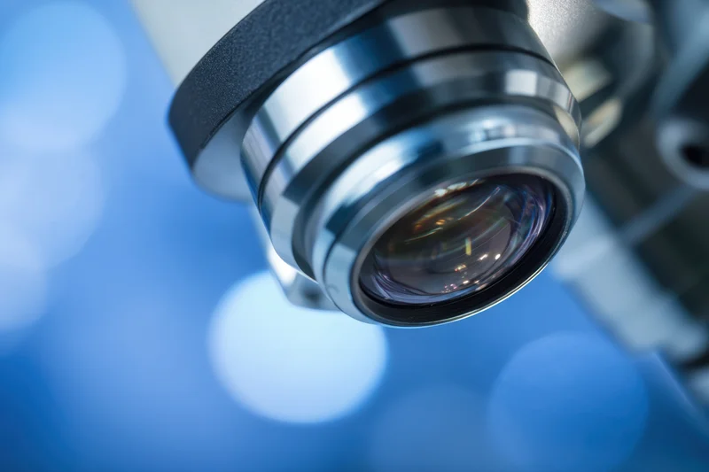 Close-up of a microscope objective lens with chrome and black housing against a blue bokeh background