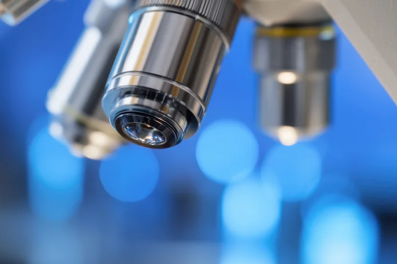 Close-up of microscope objective lens with blurred blue background