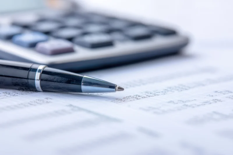 Close-up of a sleek pen resting on financial documents with a calculator in the background on a desk