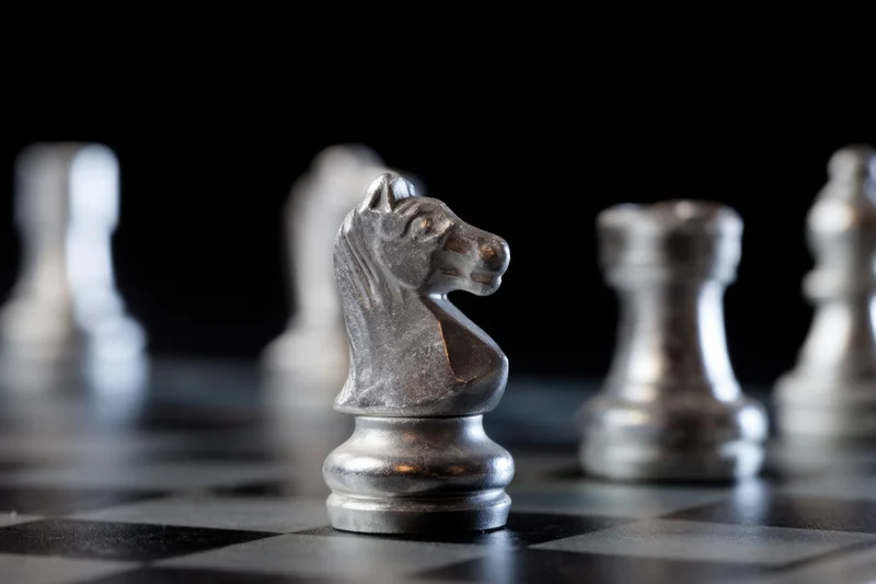 Metallic chess knight in focus on a chessboard with blurred pieces in background