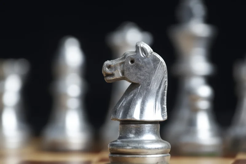 Metallic chess knight piece in sharp focus on a wooden board with blurred pieces in background
