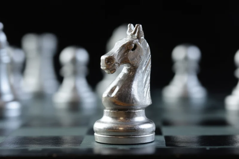 Metallic chess knight piece in focus on a checkered board with blurred pieces in background