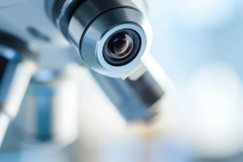 Close-up of a microscope lens with visible eyepiece and optical components in a laboratory setting