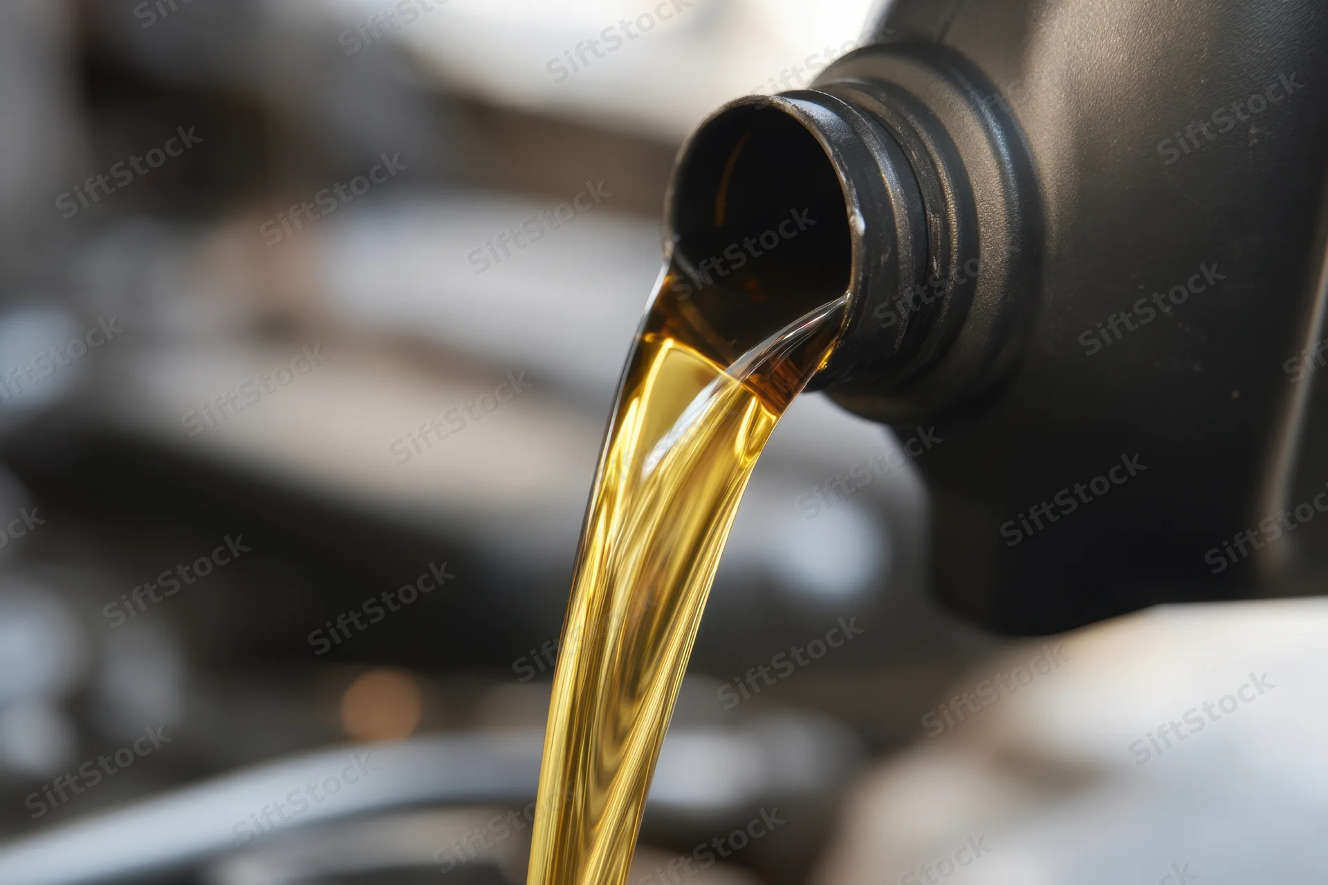 Motor oil pouring from a black bottle into an engine compartment