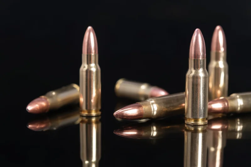 Metallic rifle cartridges arranged upright and lying on a reflective black surface