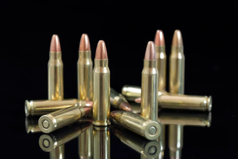 Shiny brass bullets arranged upright and lying on a reflective black surface