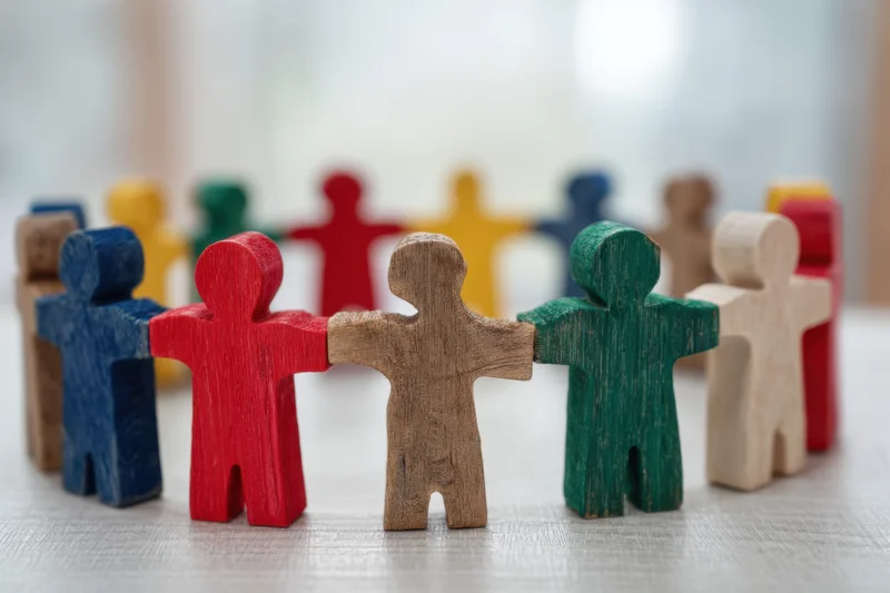 Colorful wooden figurines linked arm in arm on a light surface