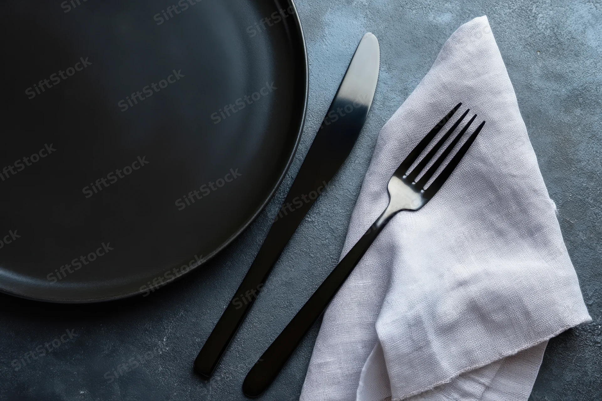 Black plate with fork and knife on napkin on dark textured tabletop