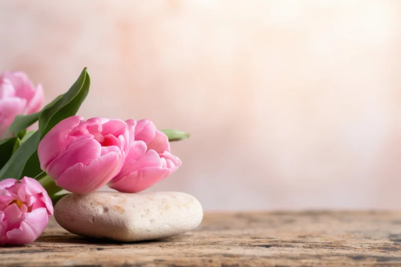 Pink tulips arranged with a smooth stone on a wooden table