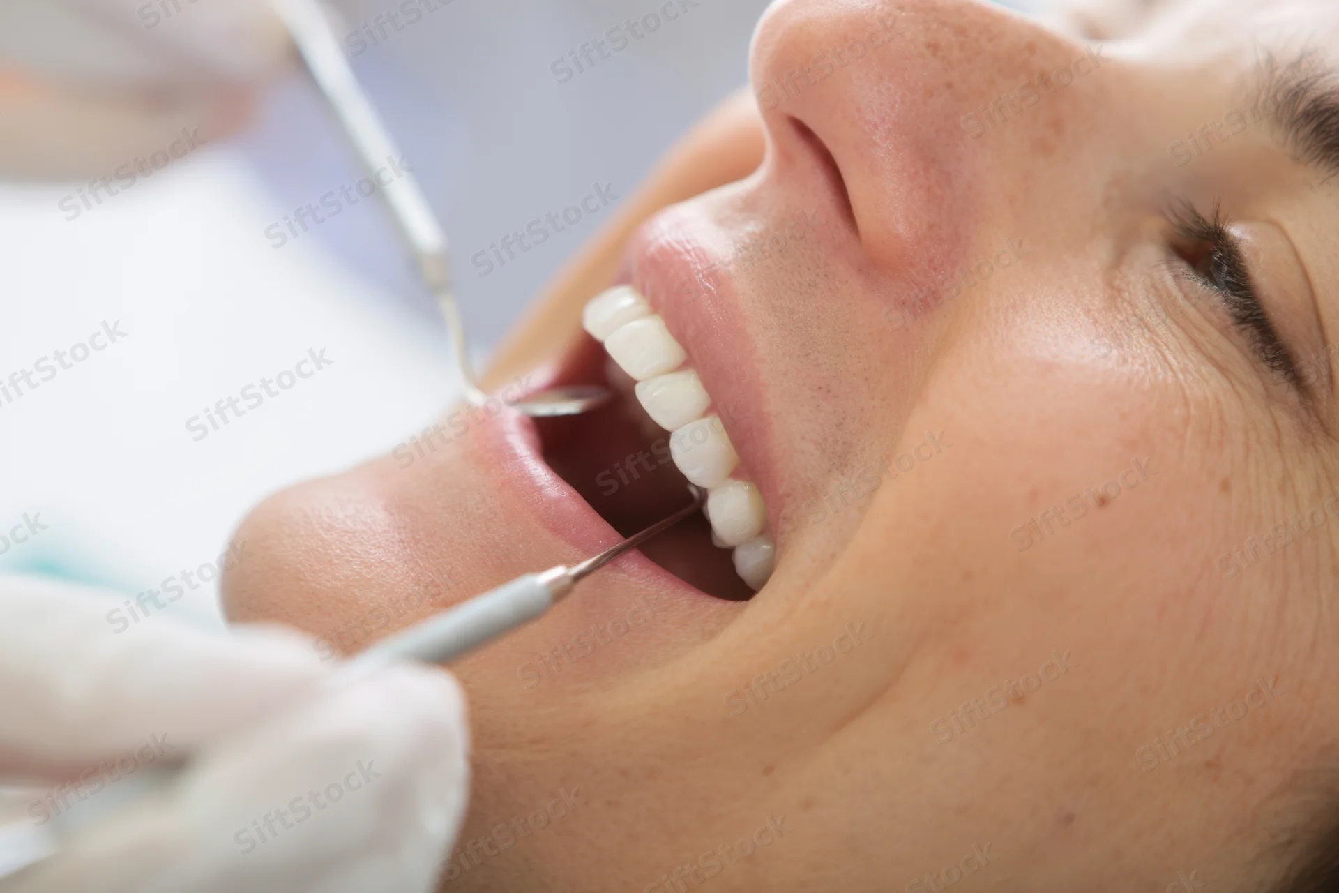 Woman undergoing dental examination with tools in her open mouth at clinic