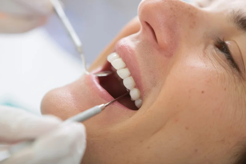 Woman undergoing dental examination with tools in her open mouth at clinic