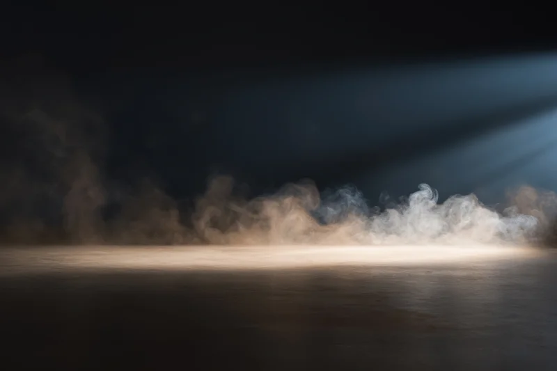 Wisps of smoke drifting over a dark smooth surface under a focused light beam