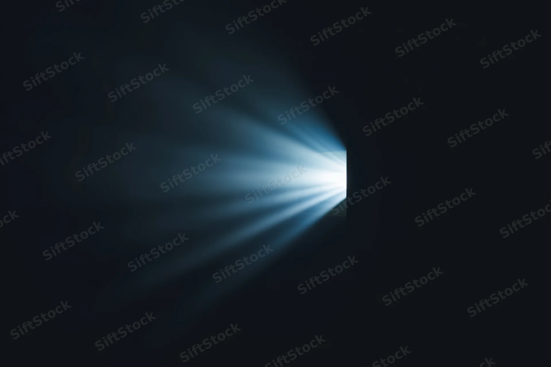 Radiant beam of light emerging from a narrow opening in darkness