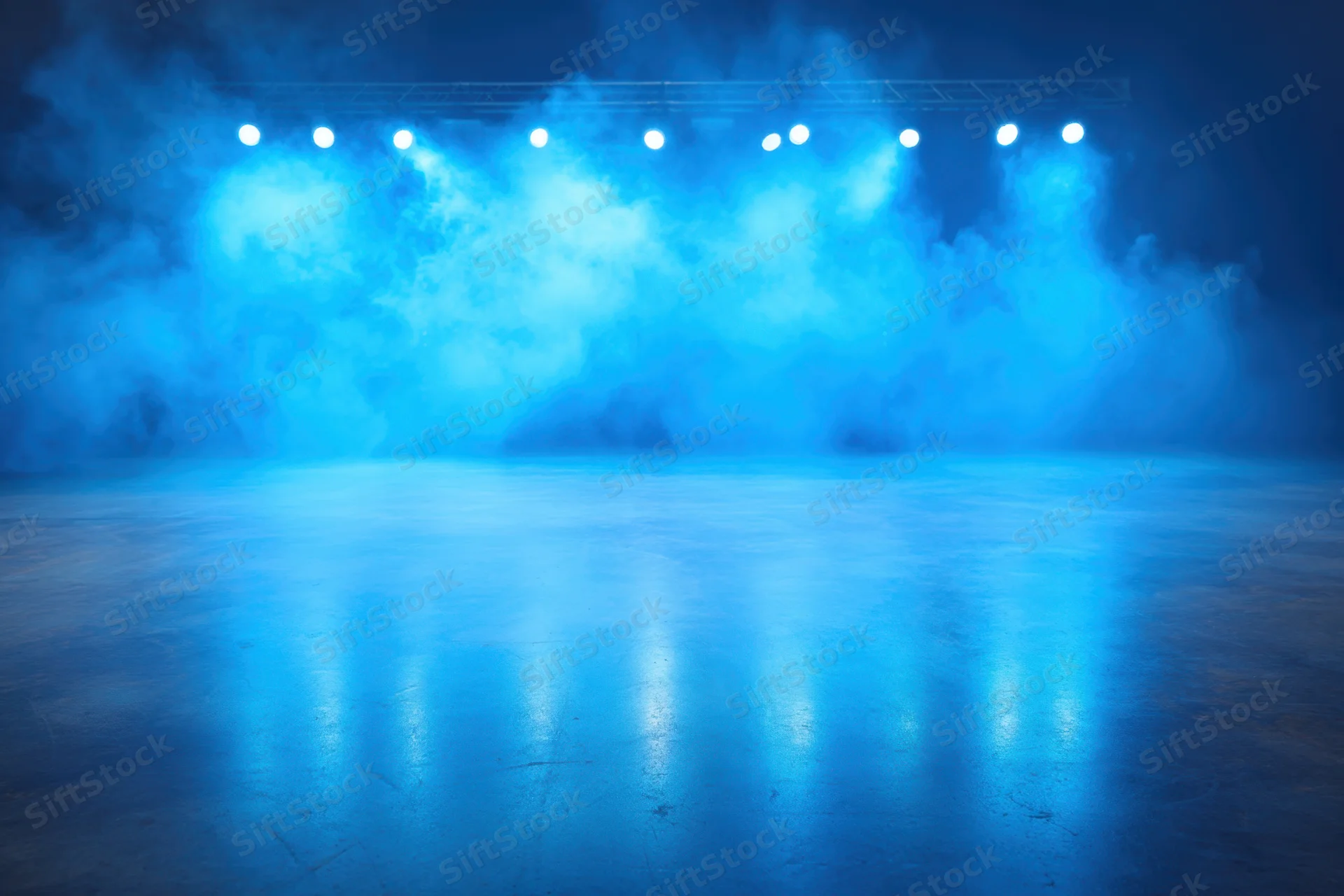 Stage illuminated by blue spotlights with smoke and reflections on the floor