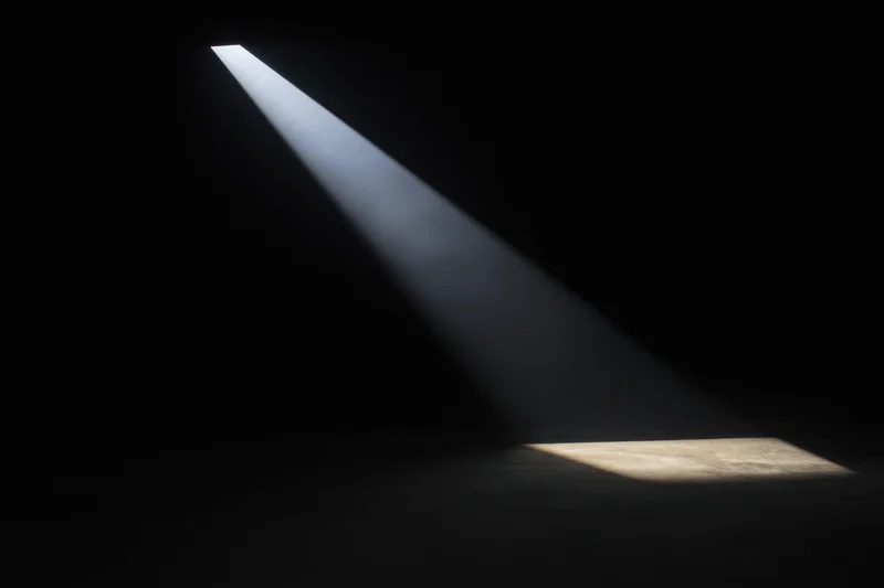 A focused beam of light cutting through a dark interior space, illuminating a patch of concrete floor