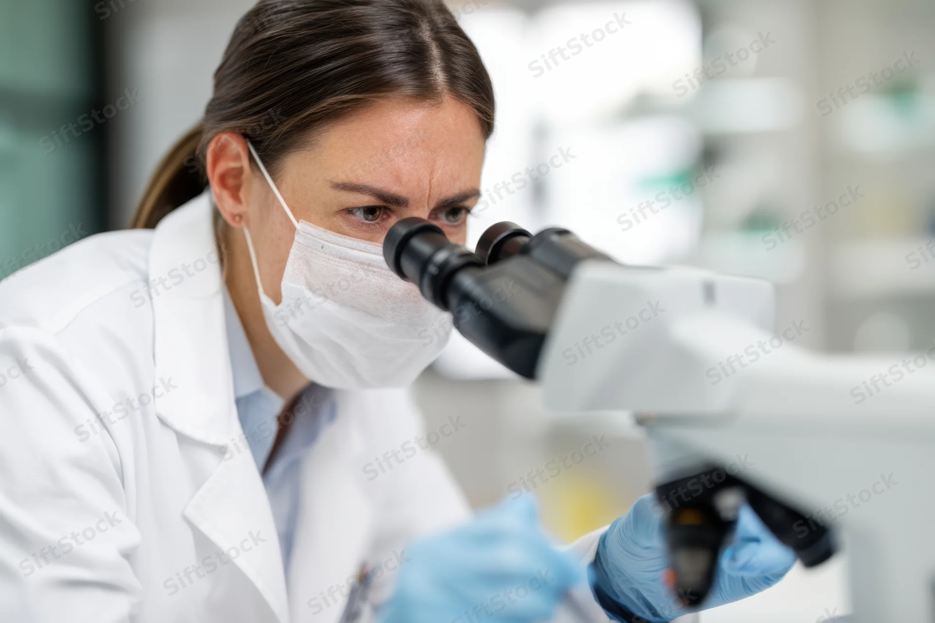 Female scientist in lab coat examining sample under microscope in laboratory setting