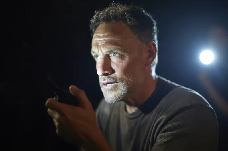 Focused man speaking into handheld radio in dark environment with spotlight behind him