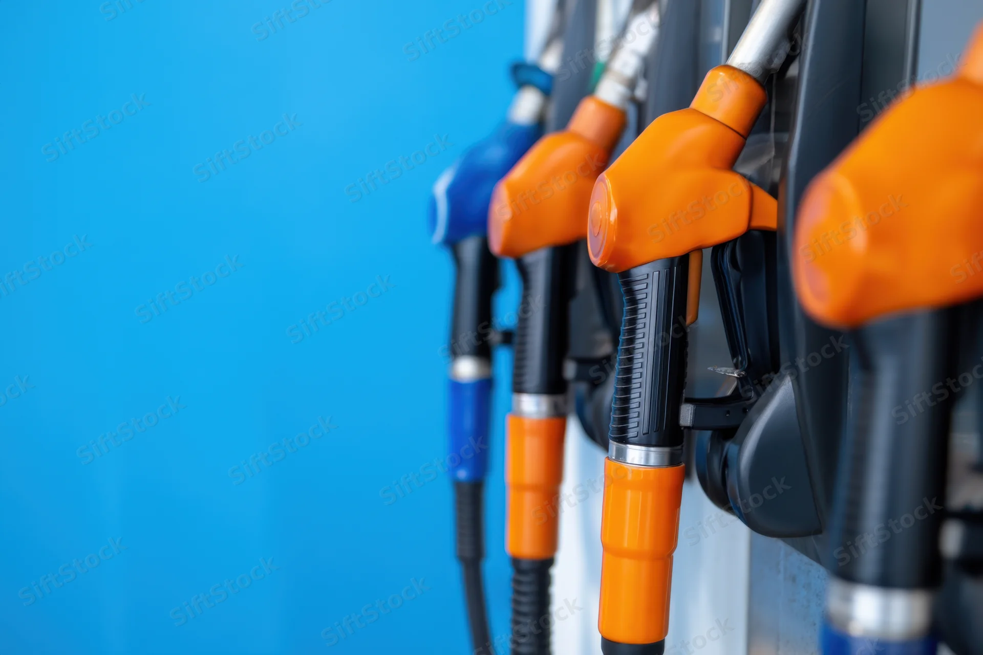 Row of fuel nozzles in orange and blue at a gas station against a blue background