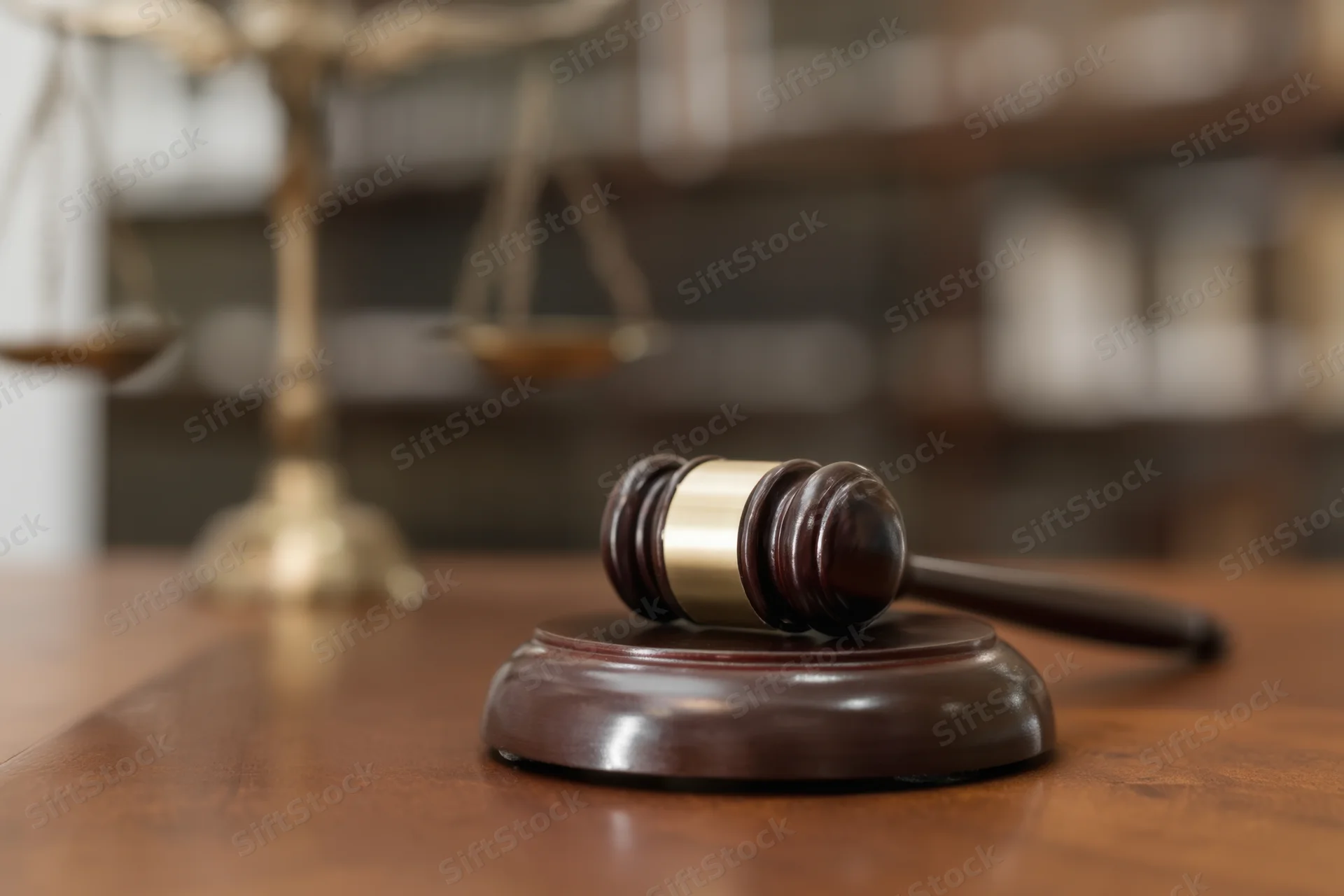 Gavel resting on wooden desk with brass scales in background