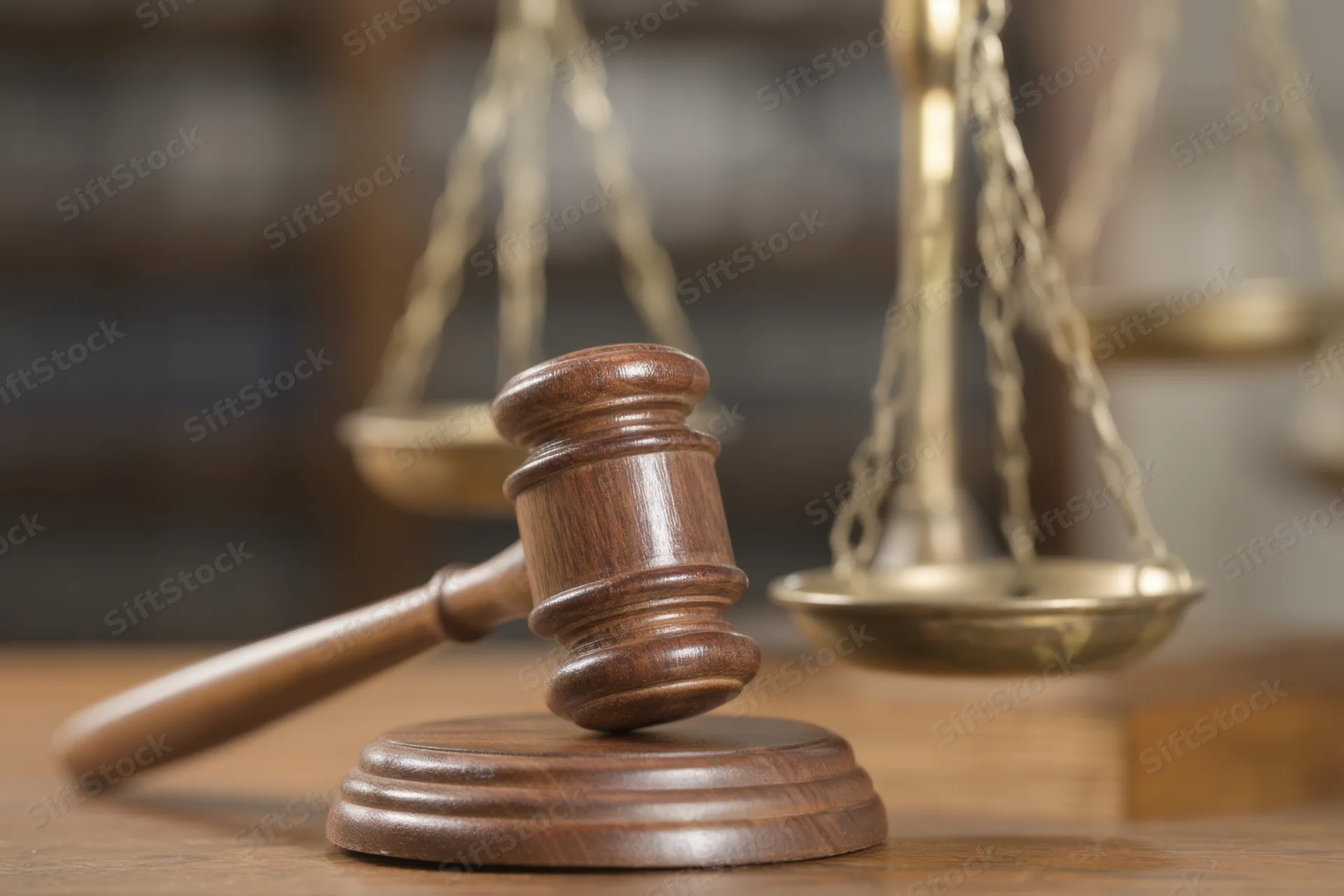 Wooden gavel resting on a desk beside brass scales of justice in a courtroom setting