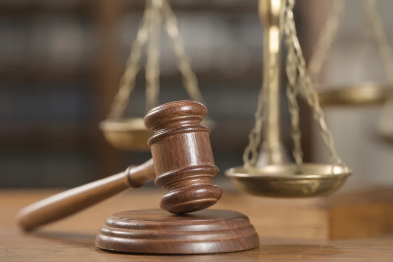 Wooden gavel resting on a desk beside brass scales of justice in a courtroom setting