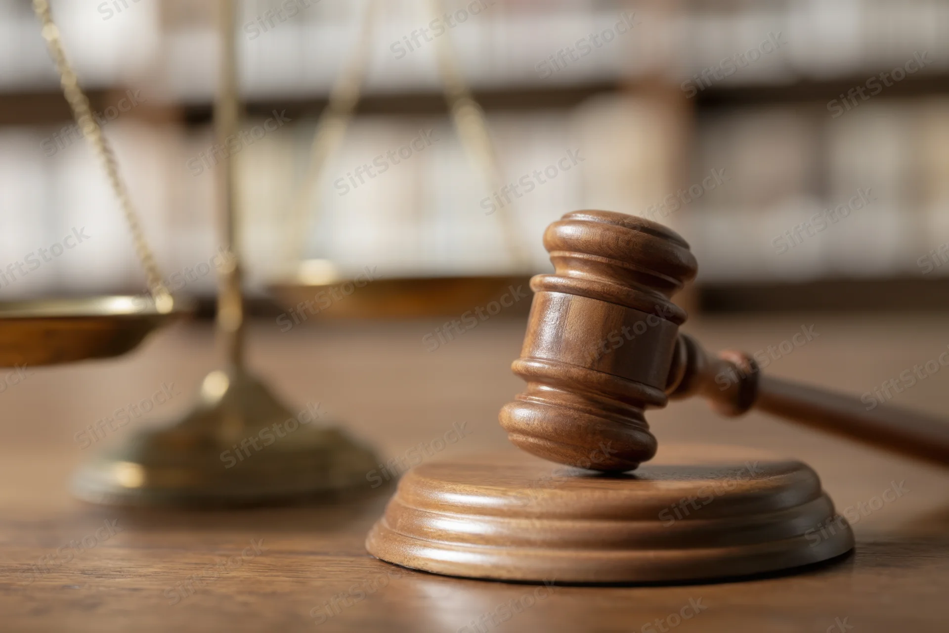 Wooden gavel resting on sound block beside brass scales on a desk