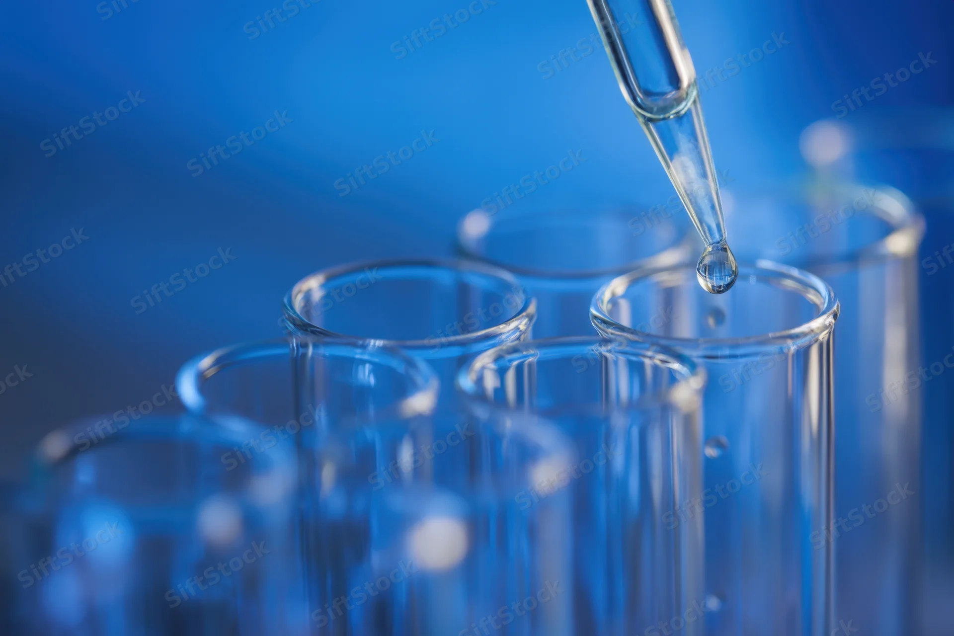 Glass pipette releasing a drop above a row of test tubes in a lab setting