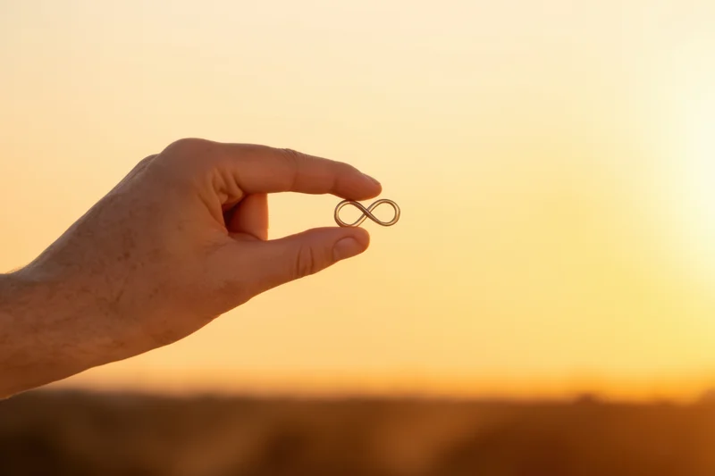 Hand holding infinity symbol against sunset sky