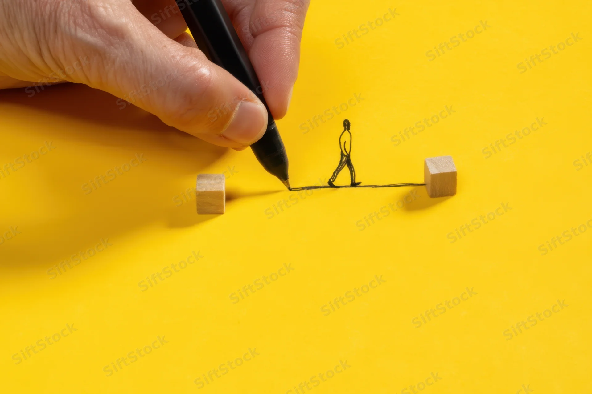 Hand drawing a line with a figure walking between two wooden cubes on yellow surface