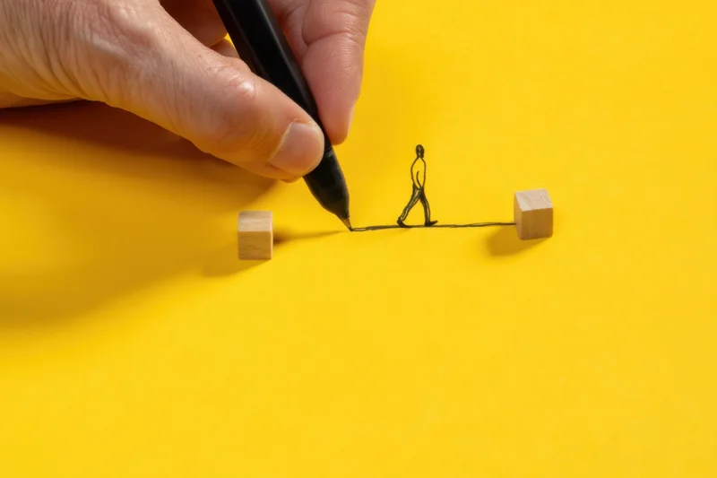 Hand drawing a line with a figure walking between two wooden cubes on yellow surface