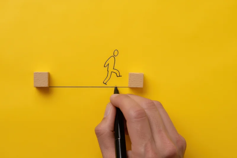 Hand drawing a line with a figure balancing on it between two wooden blocks on yellow background