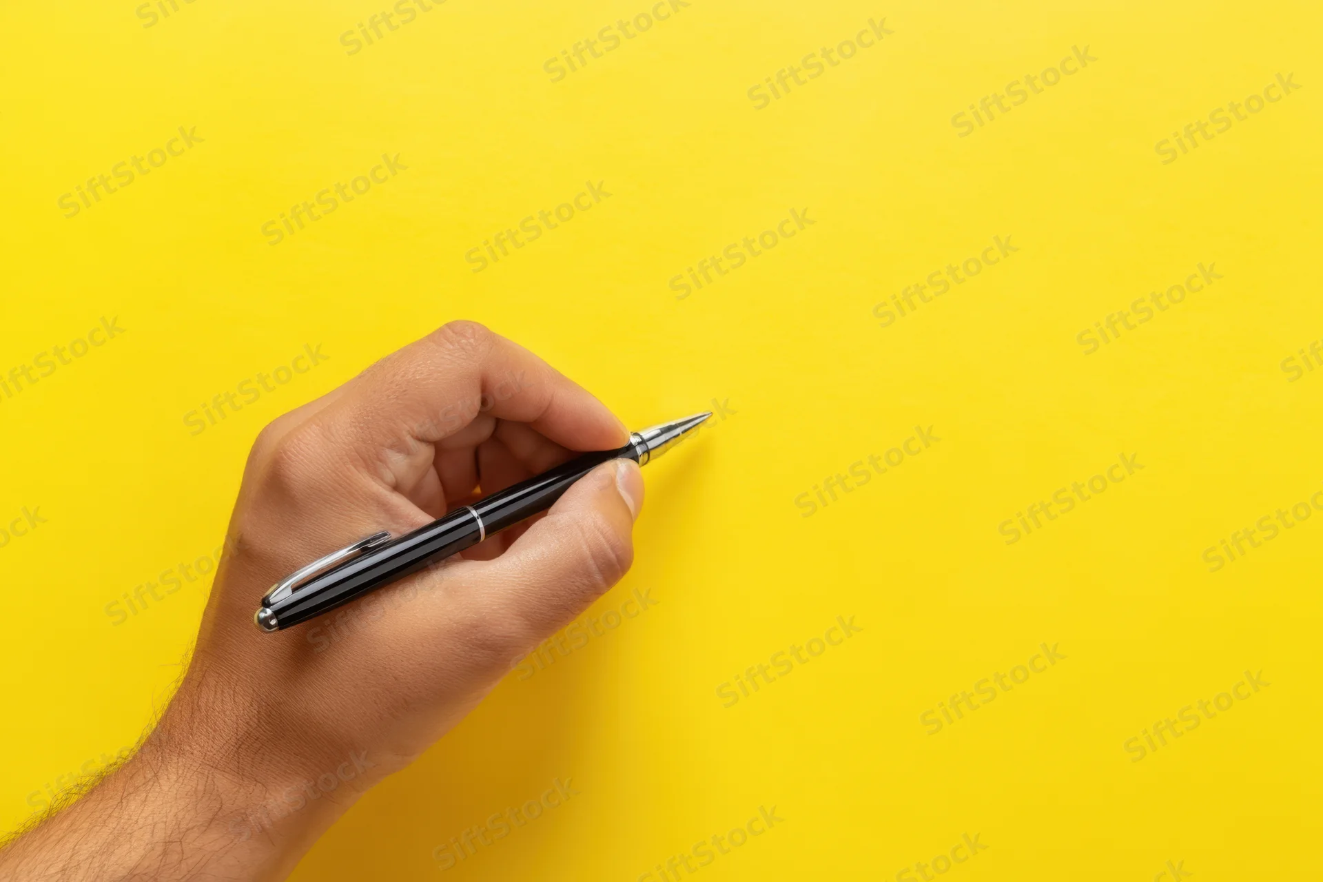 Hand holding black pen poised above vibrant yellow surface