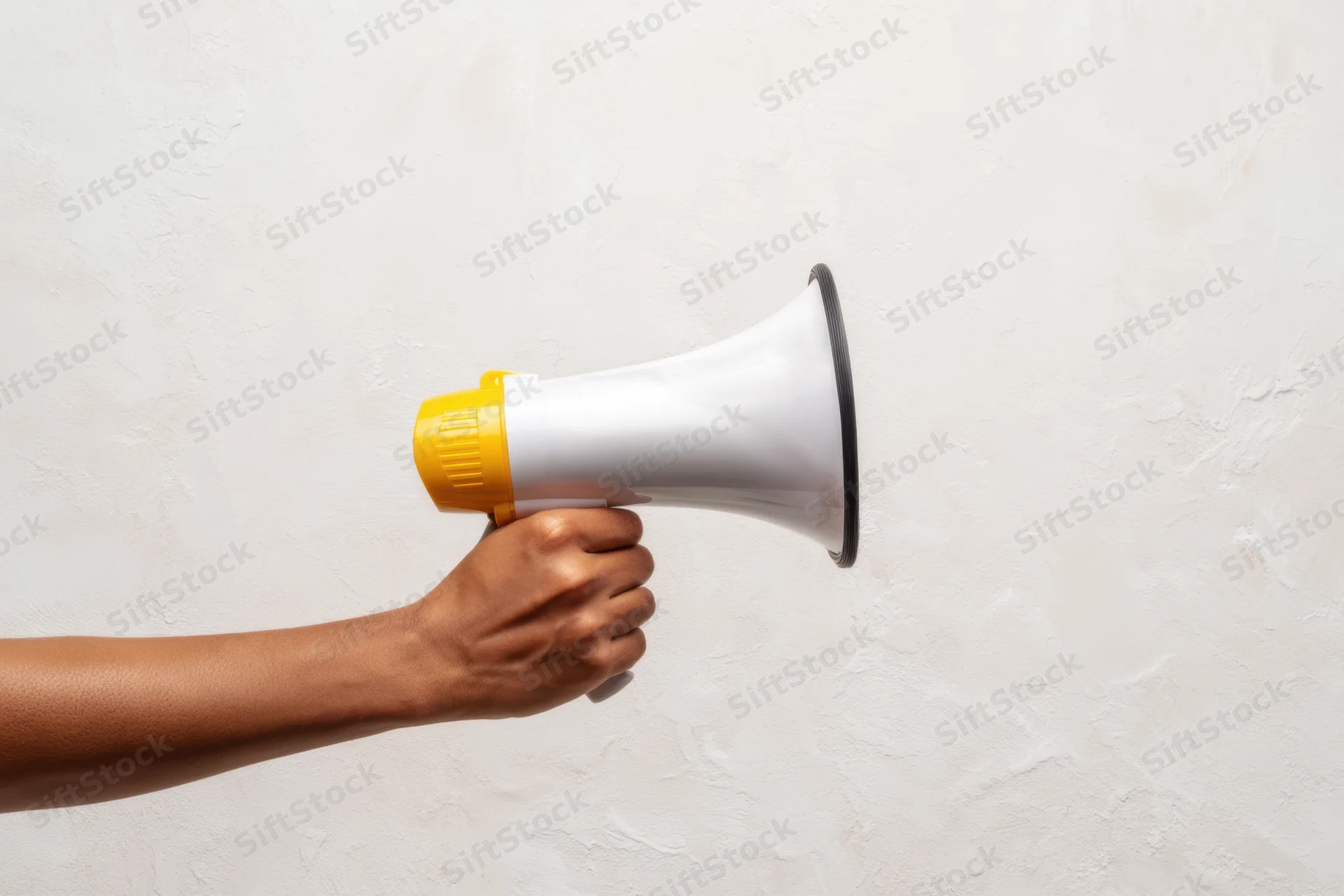 Hand holding a white and yellow megaphone against a textured white wall