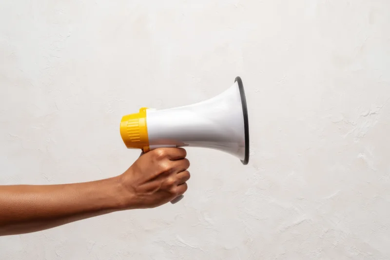 Hand holding a white and yellow megaphone against a textured white wall