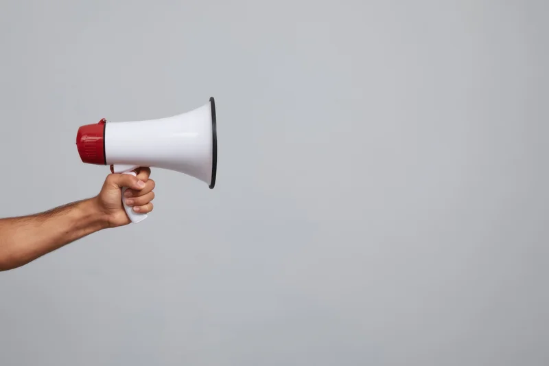Hand holding a white and red megaphone against a plain gray background