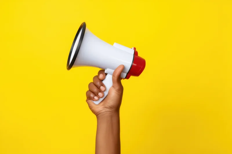Hand holding megaphone against vibrant yellow background