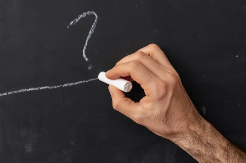 Hand holding chalk writing a question mark on a blackboard