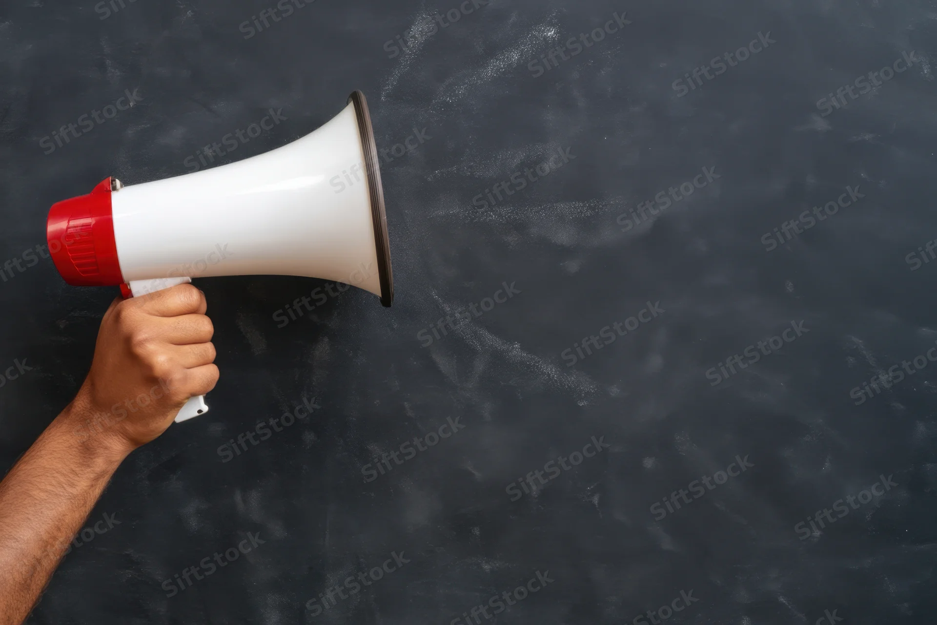 Hand holding red and white megaphone against dark chalkboard background