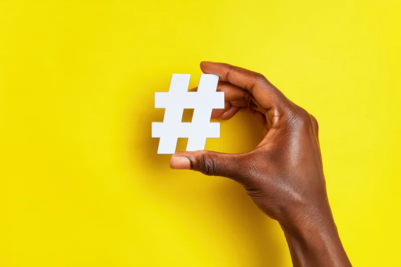 Hand holding white hashtag symbol against vibrant yellow background
