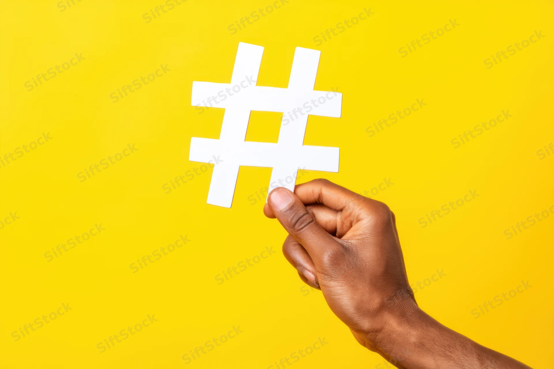 Hand holding white hashtag symbol against vibrant yellow background