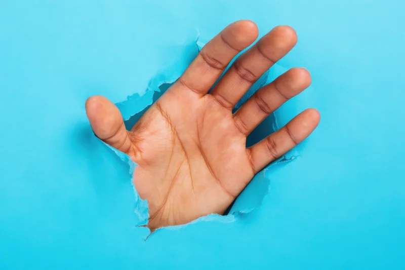 Hand reaching through torn hole in blue paper background