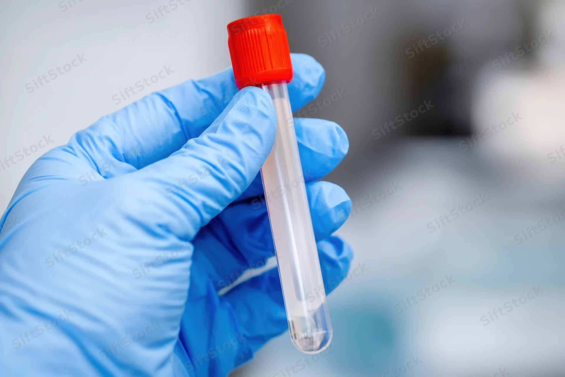 Hand in blue latex glove holding a blood collection tube in a laboratory setting