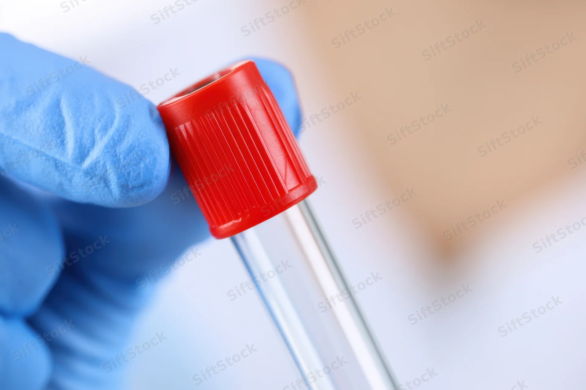 Hand in blue latex glove holding a red-capped blood collection tube in a laboratory setting