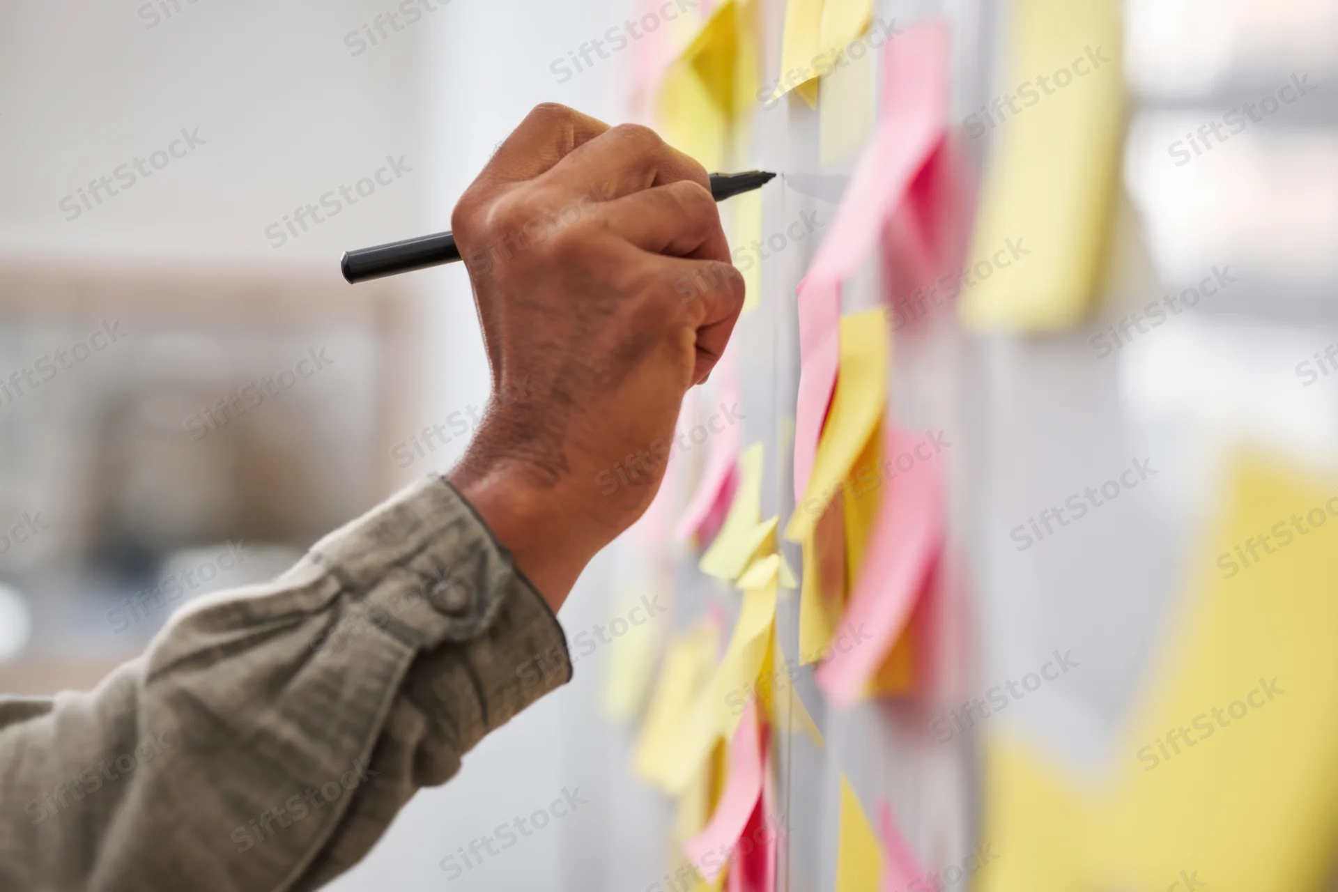 Hand writing on a transparent board with colorful sticky notes in an office workspace