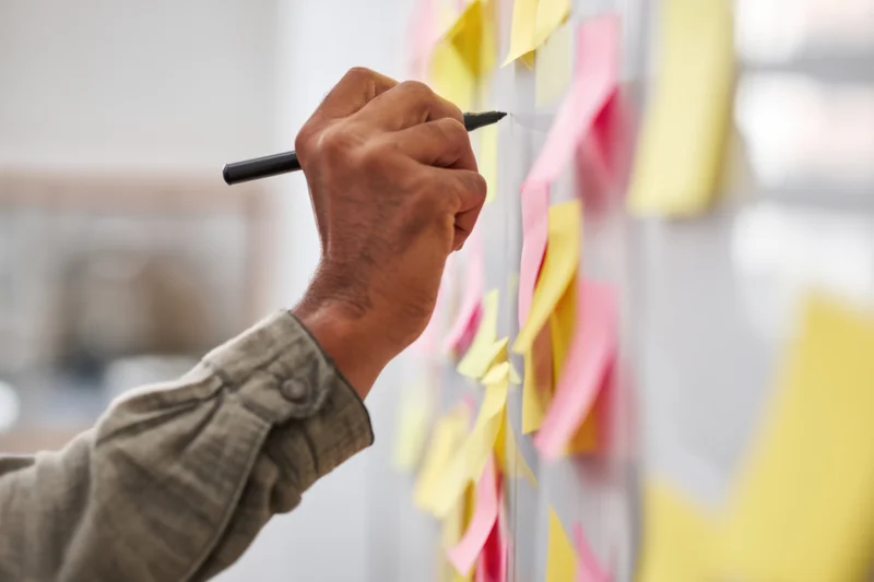 Hand writing on a transparent board with colorful sticky notes in an office workspace