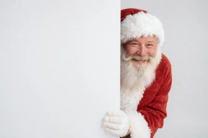 Santa peeking from behind a blank white board with copyspace
