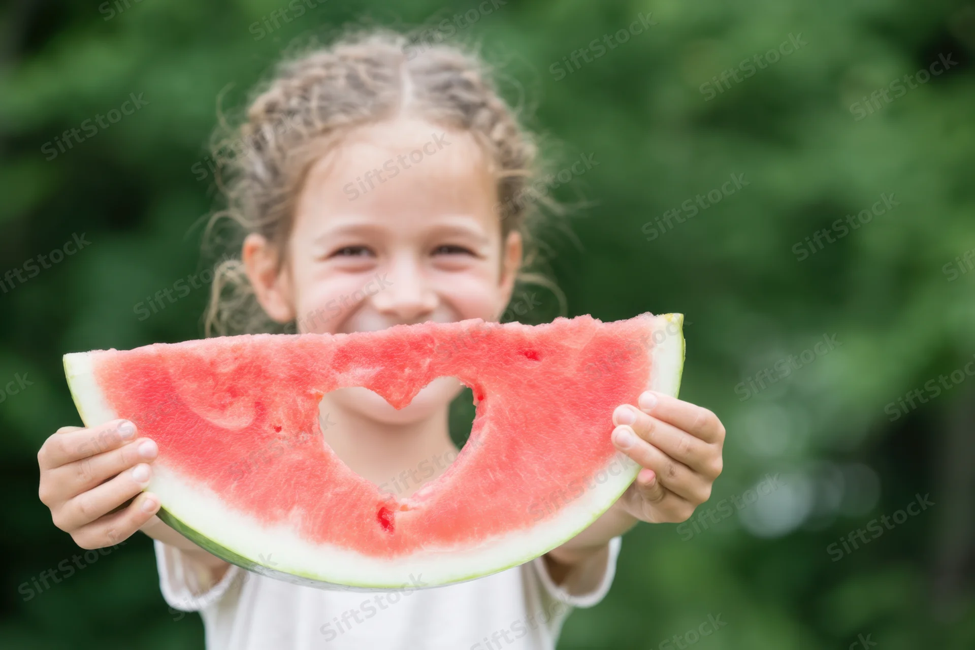 Smiling girl holding watermelon slice with heart cutout outdoors in summer garden