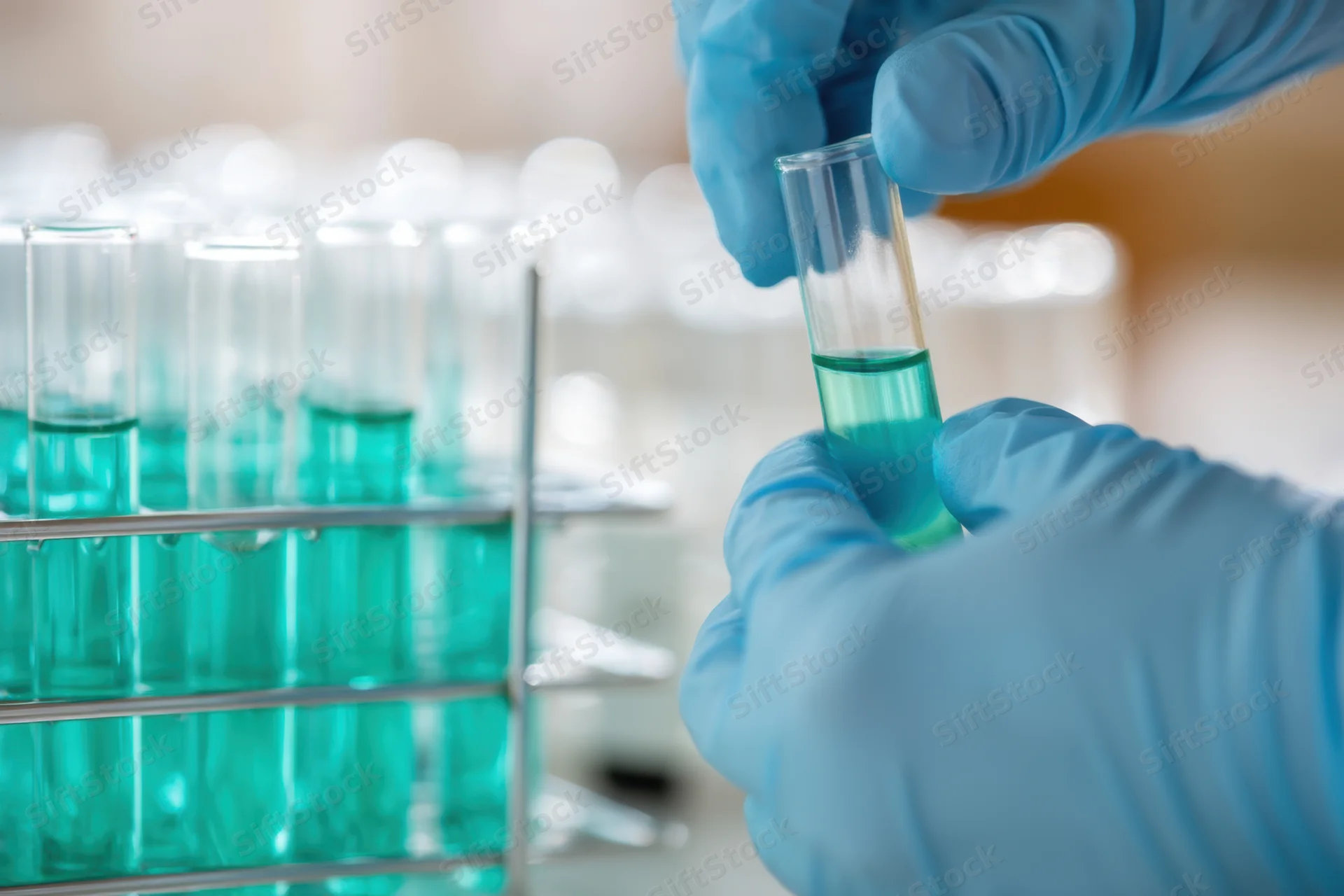 Scientist in blue gloves holding a test tube with teal fluid during laboratory analysis